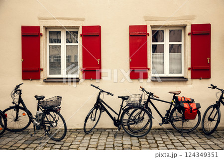 A picturesque European facade with two windows featuring red wooden shutters. Parked bicycles along 124349351