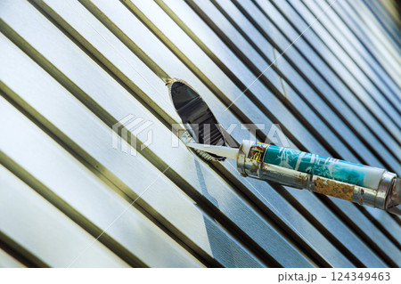 Construction worker applies caulk to pvc siding using caulking gun on ensuring secure weather proof finish. 124349463