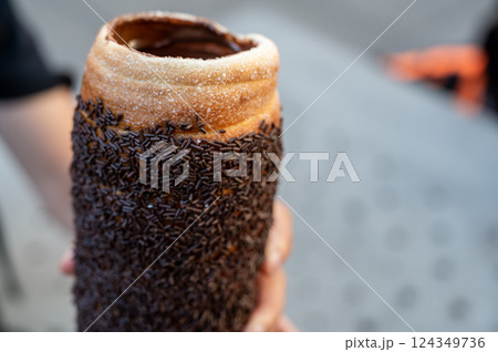 Budapest, Hungary, August 30, 2022. Close up of a Chimney cake topped with cream and chocolate pralines. Street food lifestyle. 124349736