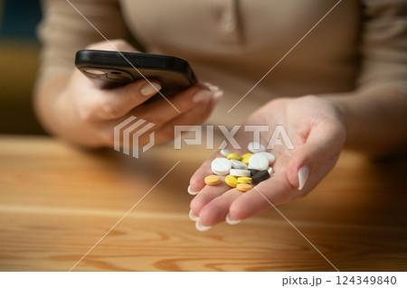 Showcasing various pills in hand while using smartphone in a cozy indoor setting Showcasing various pills in hand while using smartphone in a cozy indoor setting 124349840