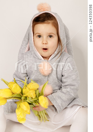 Surprised Toddler in Bunny Costume Holding Yellow Tulips on White Grey Background Surprised Toddler in Bunny Costume Holding Yellow Tulips on White Grey Background 124350398