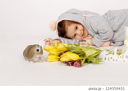 Cute Toddler in Bunny Costume Lying Next to Easter Decorations and Yellow Tulips 124350431