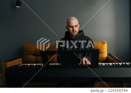 Portrait of bearded male musician plying on electric piano, composing music at home, practicing and recording new song in stylish modern apartment setting. Concept of recording music at home. 124350794