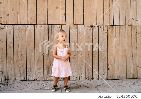 Little girl stands against the background of a wooden wall. High quality photo 124350970