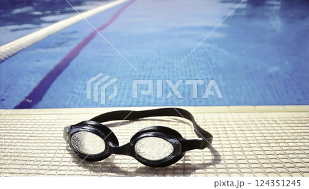 Swimming goggles on poolside tiles with crystal clear water background 124351245