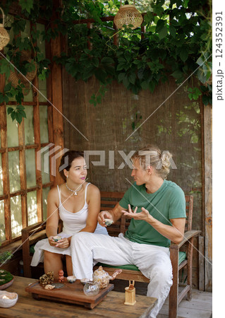 Young couple sitting in outdoor Japanese spring garden in backyard porch of zen home. Man wearing green t-shirt and white trousers and woman white dress. Man and woman have tea ceremony. 124352391