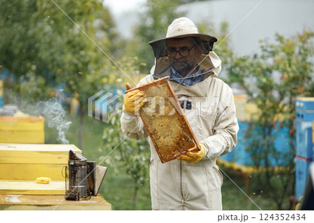Experienced senior apiarist in his apiary setting a fire in a bee smoker. Beekeeper harvesting honey. Bee smoker is used to calm bees before frame removal. 124352434