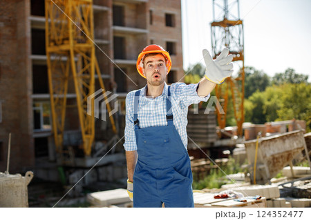 Portrait of construction site manager standing wearing orange helmet. Man giving an order to workers. Construction site on a background. 124352477