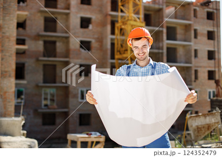 Construction site manager standing wearing helmet, thinking at construction site. Construction site on background. Man holding documents. 124352479