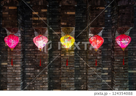 A collection of colorful lanterns beautifully hanging against a charming brick wall 124354088