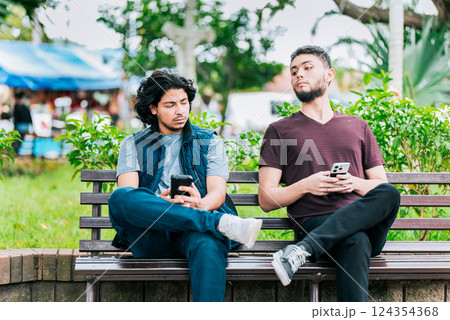 Jealous guy spying on friend's phone outdoors. Suspicious man spying on friend phone 124354368