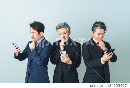 スマホを見ながら考えるミドルエイジ男性ビジネスパーソンのグループ 124355467