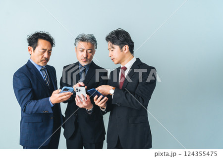 スマホの画面を見せ合うミドルエイジ男性ビジネスパーソンのグループ スマホの画面を見せ合うミドルエイジ男性ビジネスパーソンのグループ 124355475