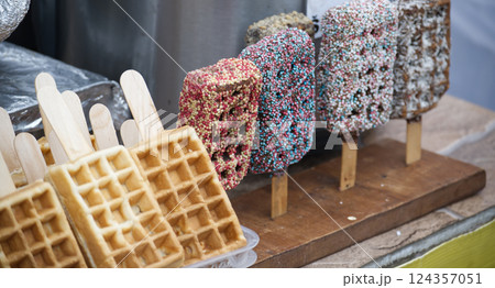 Assorted waffle and chocolate pops on sticks, arranged on a rustic wooden display 124357051