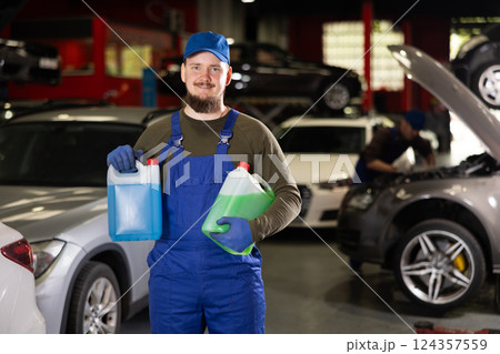 Portrait of professional auto mechanic in uniform with canisters of blue and red antifreeze in his hands 124357559
