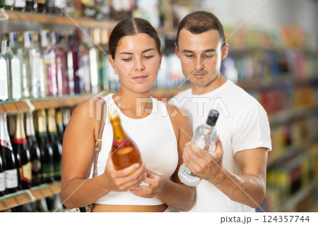 Man with wife near display of alcohol drinks in hypermarket doubt choice. Man with wife near display of alcohol drinks in hypermarket doubt choice. 124357744