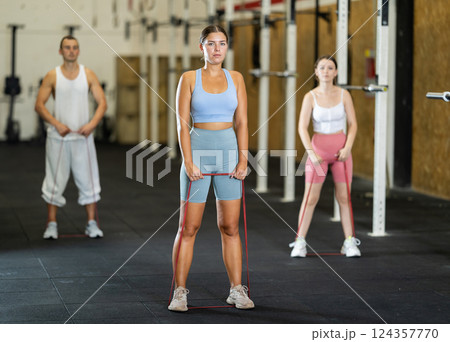 Young girl working out with other athletes with resistance band, strong biceps or abdominal muscles in gym 124357770
