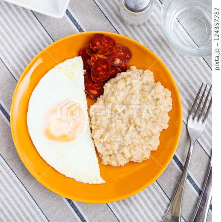 Homemade hearty breakfast - boiled oatmeal, fried eggs with chorizo sausage. Spanish dish 124357787