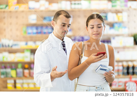 In pharmacy girl customer scans QR code on label box, photographs packaging in presence of employee In pharmacy girl customer scans QR code on label box, photographs packaging in presence of employee 124357818