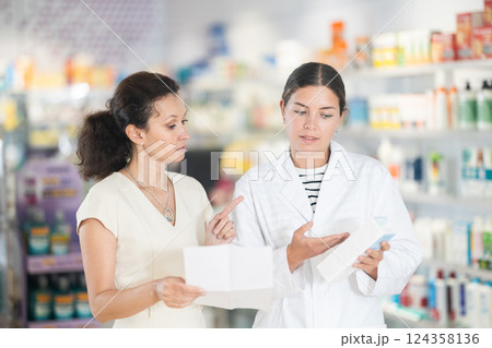 Female pharmacist helping woman with prescription choosing medical supplies at drugstore Female pharmacist helping woman with prescription choosing medical supplies at drugstore 124358136