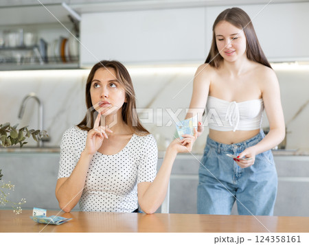 Thoughtful mother sitting at the kitchen table giving money to daughter Thoughtful mother sitting at the kitchen table giving money to daughter 124358161