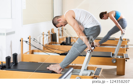 Focused man practicing exercises on Pilates reformer in studio Focused man practicing exercises on Pilates reformer in studio 124358207