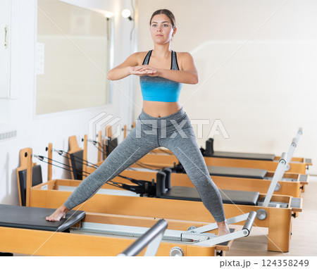 Young girl performing pilates exercises on reformer in studio 124358249