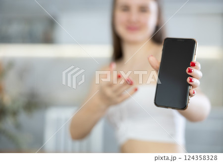 Young woman posing with phone in kitchen Young woman posing with phone in kitchen 124358328