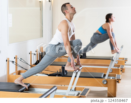 Sporty man in sports wear engages in Pilates on reformer machine Sporty man in sports wear engages in Pilates on reformer machine 124358467