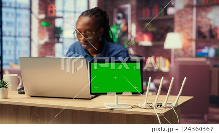 African American female freelancer browse troubleshooting guide next to copy space, working on debugging router issues to restore home network. Young woman struggles to solve tasks. Camera B. 124360367