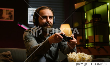 Excited man playing videogames using controller, having fun in neon illuminated room. Enthusiastic gamer competing in multiplayer game using gamepad, talking with friends through headset, camera A 124360380