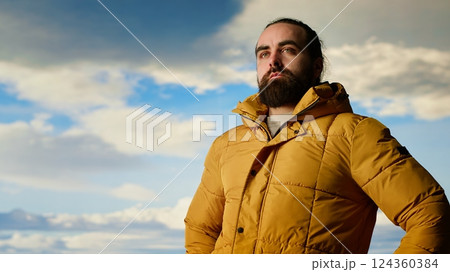 Nature lover stands at the edge of a breathtaking mountain range, looking at the scenic background of towering peaks and vast sky. Young man enjoying adventure and outdoor exploration. Camera B. Nature lover stands at the edge of a breathtaking mountain range, looking at the scenic background of towering peaks and vast sky. Young man enjoying adventure and outdoor exploration. Camera B. 124360384