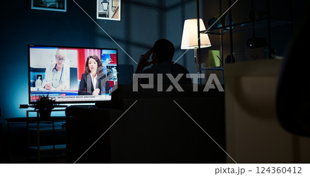 Curious spectator reading news coverage titles on smart tv set, sitting on couch and listening to journalist lay out recent global events. Guy watching daily news headlines, tv content. Camera A. 124360412