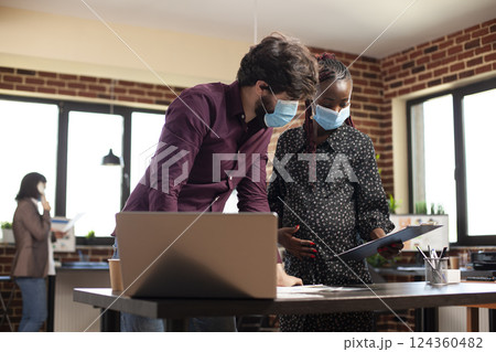 African american woman with baby bump presents strategy plan on clipboard to businessman in casual office. Pregnant lady and caucasian coworker with laptop at desk, doing research for startup company. African american woman with baby bump presents strategy plan on clipboard to businessman in casual office. Pregnant lady and caucasian coworker with laptop at desk, doing research for startup company. 124360482
