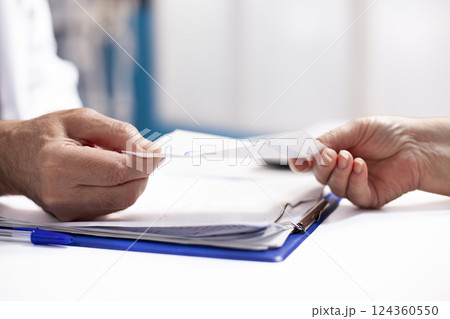 Closeup of caucasian healthcare provider in lab coat presenting prescription form to patient. Detailed focus on two individuals holding medical document with clipboard visible on the table. 124360550