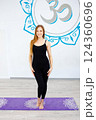 Smiling woman in black sportswear standing on a yoga mat  124360696