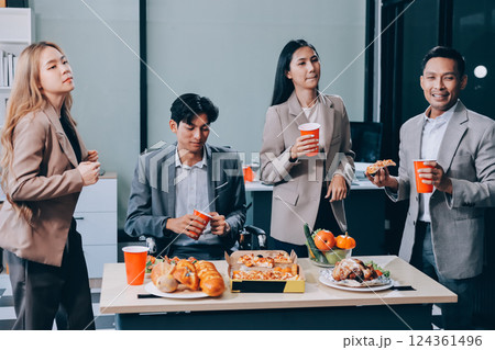 Asian office colleagues and friends enjoy a daytime BBQ with pizza and beer, celebrating Halloween and cheering for their favorite soccer team, creating a lively atmosphere filled with joy. 124361496