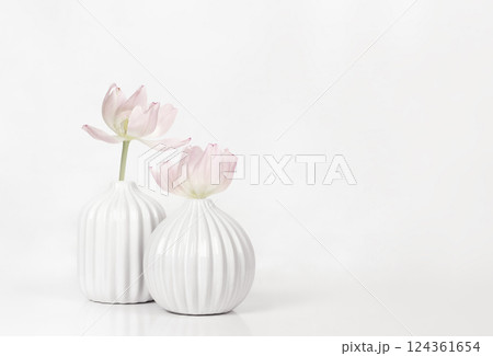 Two white textured vases with pink fading tulip flowers on white table Two white textured vases with pink fading tulip flowers on white table 124361654