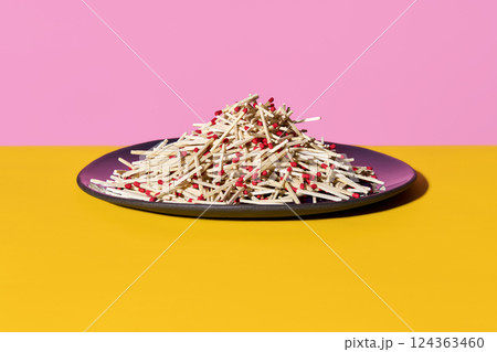 Pile of red-tipped matches on purple plate over colorful background Pile of red-tipped matches on purple plate over colorful background 124363460