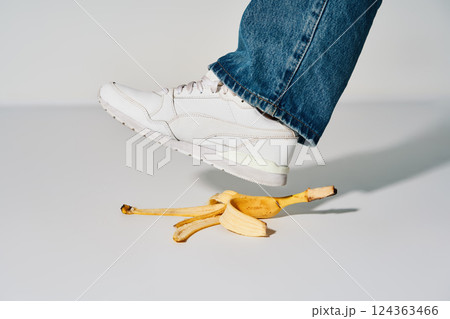 Foot stepping on banana peel over white background, 124363466