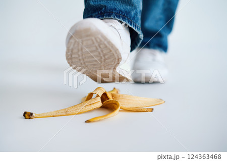 Foot stepping on banana peel over white background, 124363468