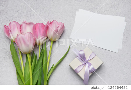 Pink tulips bouquet, gift box and blank cards creating festive composition on table 124364422