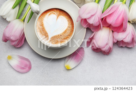 Cappuccino with heart shaped foam and pink tulips bouquet on grey table 124364423