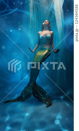 Mysterious elegant young woman, mermaid with golden tail, covered in flying fabric, floating against dreamlike ocean background 124364588
