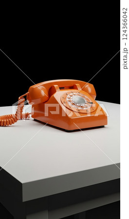 Vintage orange rotary phone on white table against black background 124366042