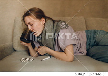 Young woman wearing scarf with pillow drugs medicine has flu ill sick disease cold at home indoor on sofa 124366455