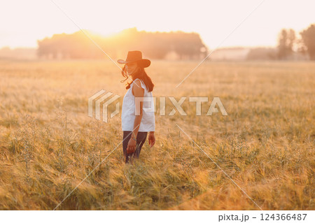 Woman farmer in cowboy hat at agricultural field on sunset. 124366487