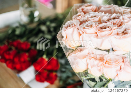 Soft peach roses wrapped in bouquet paper with red roses in the background. Represents floral subscription services, bouquet gifting, and recurring flower deliveries 124367279