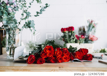 Red rose bouquet ready for packing in florist studio with eucalyptus in vase. Reflects monthly floral subscriptions and romantic gifting rituals 124367280
