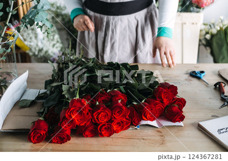 Florist standing behind bunch of red roses during bouquet preparation. Represents small floral business, intentional design, and craft-focused entrepreneurship 124367281